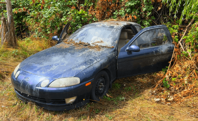 Dark blue 1993 Lexus SC400 pulled into overgrown brush with the driver door open.
